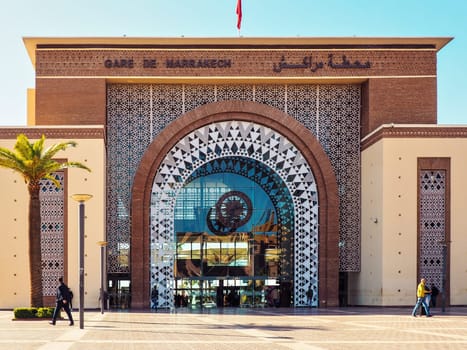 Marrakech, Morocco - January 02, 2020: Ornaments decorating walls of Marrakesh railway station, sun shines on pavement leading to large glass entrance, palm at side