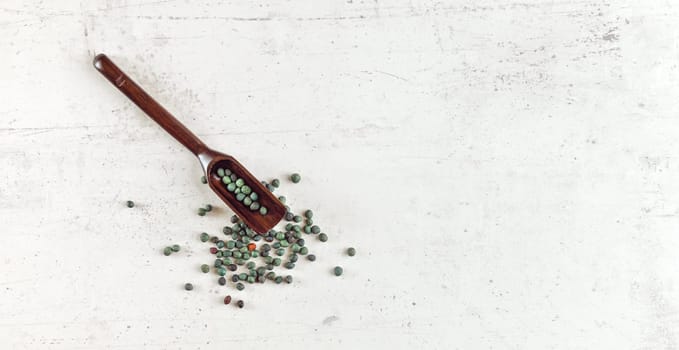 Small blue green peppercorns in dark wooden spoon on white stone like table