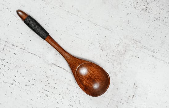 Small spoon made of dark wood, on white working board, view from above