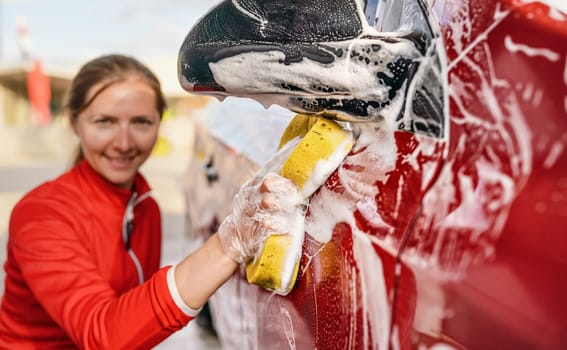 Young woman cleaning side of her car, detail on hand in glove holding yellow sponge