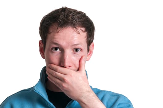 Frontal head portrait of a young brunette Caucasian man covering his mouth with his left hand while looking at the camera in shock isolated on white.