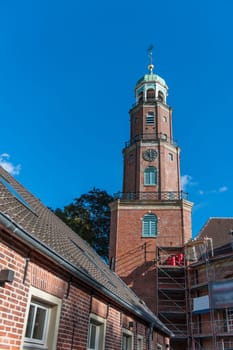 Bell tower of the large reformed church with scaffolding for maintenance work in East Frisia in autumn 2022 in sunny weather with blue sky.