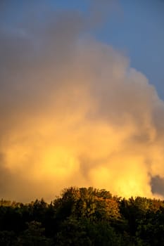 Big yellow cloud in the sky in the evening sun over a green forest