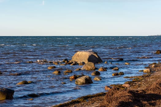 Big stones lie in the water on the Baltic Sea coast, with waves and horizon