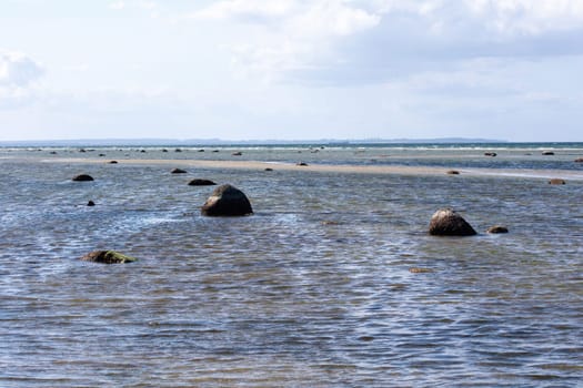 Big rock with stones lie in the water, at low tide on the coast of the Baltic Sea