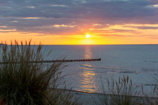 Sunset over the sea, with sand dunes, blurred beach grass and breakwaters