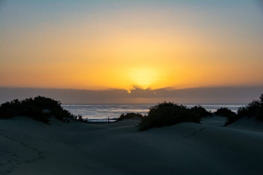 Sand dunes and sea in Maspalomas at sunset on Gran Canaria in Spain. The huge sand dunes resemble a small desert and are a nature reserve.