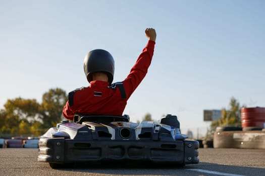 Happy go-cart driver raising hand up rejoicing and celebrating win. Carting extreme sports competition and victory in championship