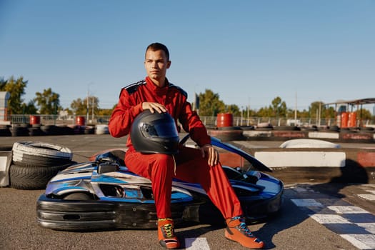 Handsome man driver with helmet sitting at his go-kart car waiting for start of competition. Professional auto sport and masculine hobby concept