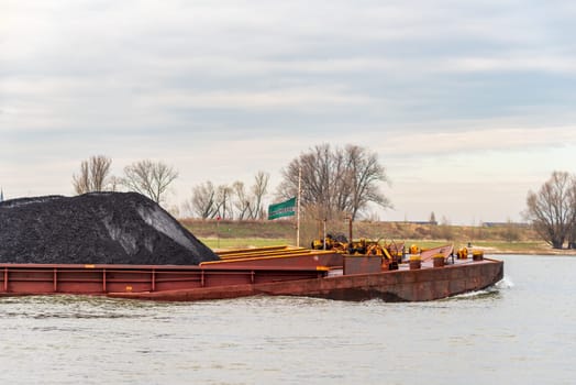 NIJMEGEN, NETHERLANDS - MARCH 9, 2024: Enormous dutch barge navigating the Waal river with a load of black sand