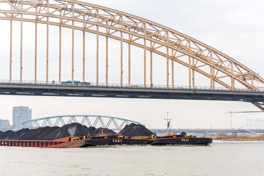 NIJMEGEN, NETHERLANDS - MARCH 9, 2024: Enormous dutch barge navigating the Waal river with a load of black sand