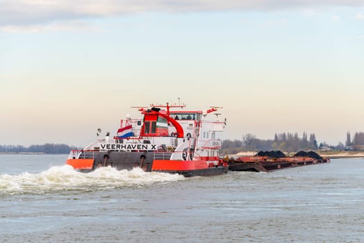 NIJMEGEN, NETHERLANDS - MARCH 9, 2024: Enormous dutch barge navigating the Waal river with a load of black sand