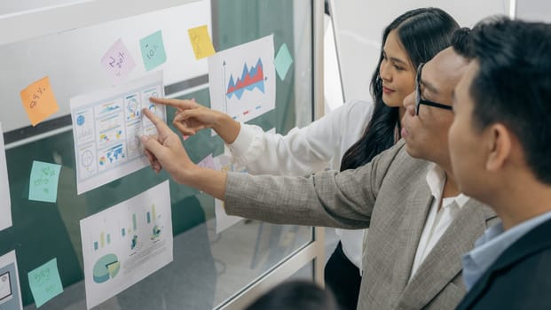 A group of people are looking at a large board with graphs and charts. One of the people is pointing to a specific area on the board