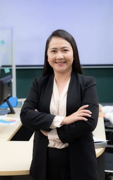 A woman in a black suit and white shirt is smiling and standing with her arms crossed. She is confident and professional