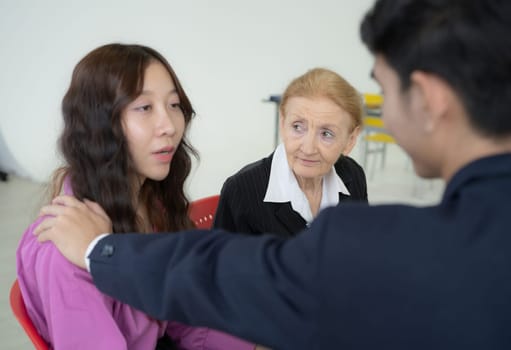 A woman is comforting a young girl. A man is standing behind them. The woman is wearing a purple shirt