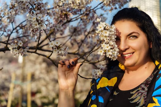 Young plus size woman smiling while covering half of her face with cherry blossom branch in spring while walking in the park.