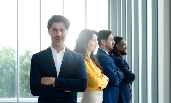 A group of four people in suits and ties are standing in a room with a window. They are all looking at the camera and appear to be posing for a photo. Scene is professional and serious