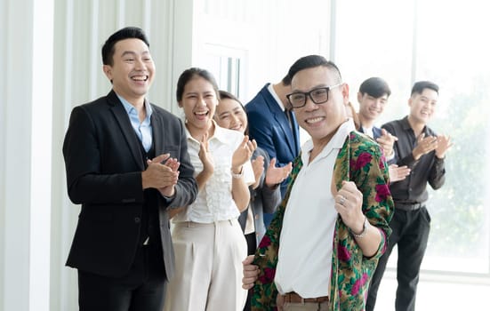 A group of people are smiling and clapping, with one man in a floral shirt standing out. Scene is happy and celebratory
