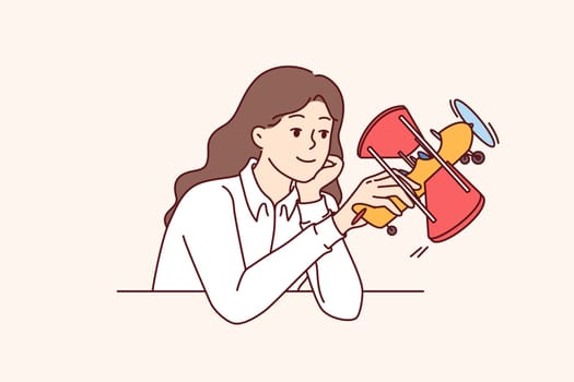 Business woman dreams of launching startup from airline industry, holding toy airplane sitting at table. Girl planning to launch airline company providing aircraft flight training services.