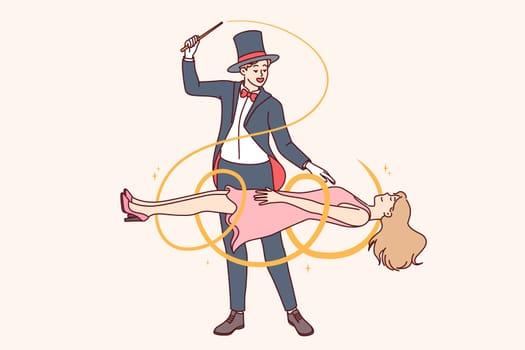 Man magician demonstrates magic trick by making woman assistant levitate during circus performance. Guy magician dressed in tuxedo and classic hat, entertaining audience with mysterious tricks