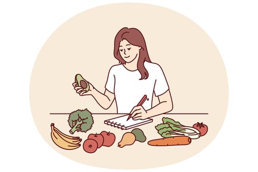 Woman near table with vegetables makes notes in notebook counting calories or making plan for new keto diet. Girl takes care of diet by choosing only organic vegetables grown by farmers