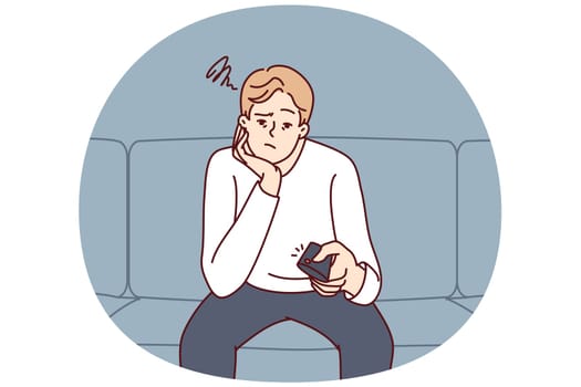 Bored man holding TV remote due to lack of satellite TV channels with interesting shows. Concept frustration and procrastination associated with lack of motivation caused by emotional burnout