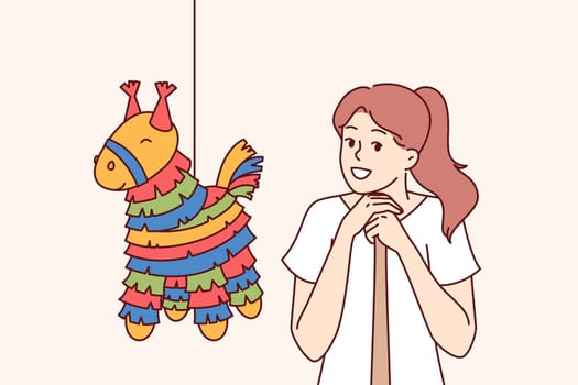 Pinata with candy near girl with bat, preparing to smash horse-shaped toy for birthday parties. Traditional mexican pinata for children party, with rope for hanging on tree branch.