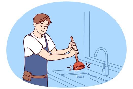 Man plumber uses plunger to clear blockage in sink in kitchen or bathroom. Guy working as plumber is dressed in overalls and is engaged in elimination breakdown associated with debris stuck in pipe