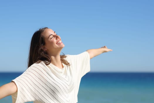 Happy woman celebrating a good day outstretching arms on the beach