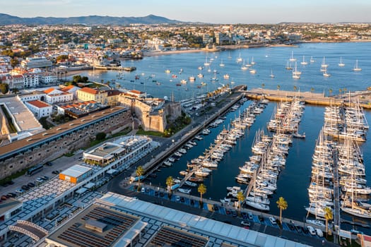Drone view Cascais, coastal town, marina near Lisbon at sunny summer evening, drone point of view. Waters of the Atlantic Ocean, rocky coastline, sailboats, yachts, catamarans moored by jetties, low sun, luxury and leisure.