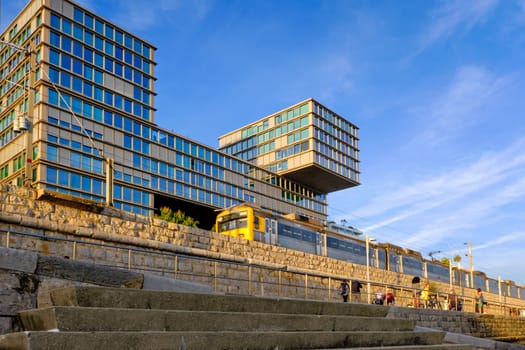 FEB 17, 2024 - Cascais, Portugal: Train from Lisbon passing by Estoril Sol Residence, luxury block of apartments by waterfront on sunny day, clear blue sky and clouds. Modern architecture by Goncalo Byrne Arquitectos