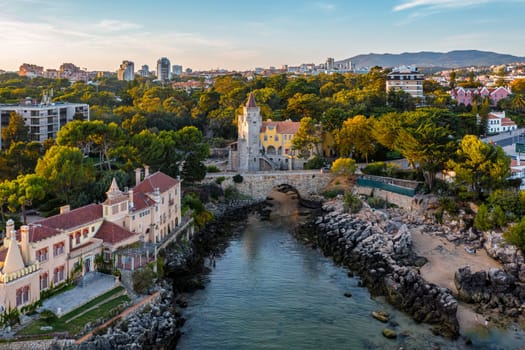 Wide shot of colorful sunset over Museum of Conde de Castro Guimaraes, Cascais, Portugal. Beautiful building in picturesque location, next to tidal pool, sandy beach, rocky shores and bridge, stylized as Manueline castle.