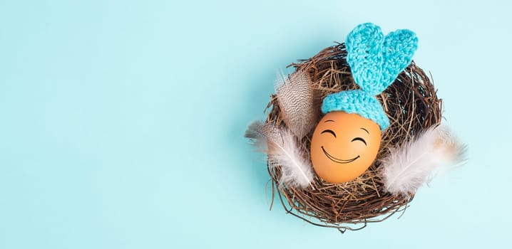 Easter bunny or rabbit egg in a bird nest, crocheted ears and feathers, spring holiday, blue color