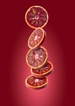 Round pieces of blood orange levitate on a red background, juicy fruit
