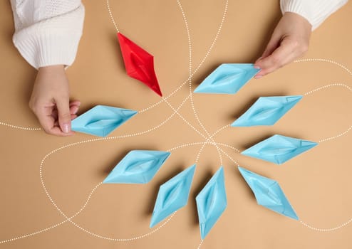 Paper boats with different trajectories in a woman’s hand on a brown background, the concept of choosing a path of movement