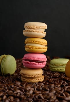 Stack of multi-colored macarons on a background of coffee beans, black background