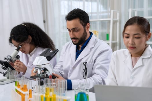 Laboratory research scientist team working on medical experiments by use of microscope and scientific data analysis on laptop.