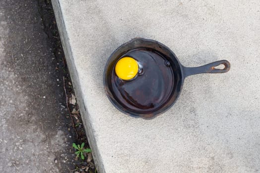 Raw egg in a frying pan on the hot asphalt road, fried food on the sidewalk, hot weather concept, summer temperature