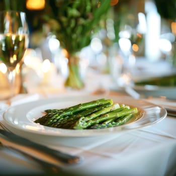 The image shows grilled asparagus on a plate. The sophisticated dining setting includes wine glasses to create an air of sophistication