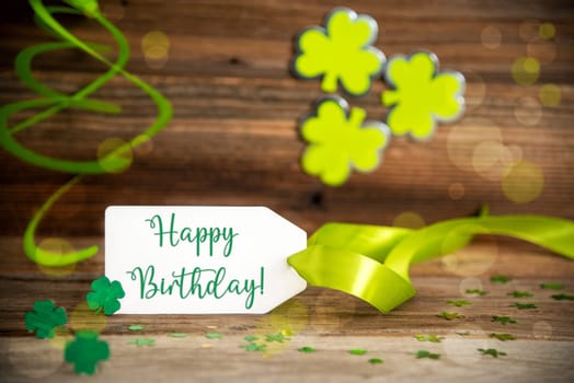 White Label With English Text Happy Birthday. Saint Patrick's Day Decoration With Green Shamrock And Clover. Wooden Vintage Background With Festive Ribbon.
