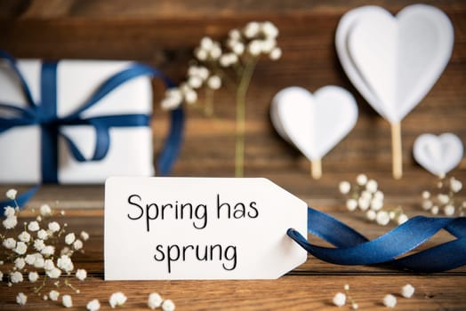 Label With English Text Spring Has Sprung. White Festive Decoration Like Present With Blue Bow, Heart and Flowers. Vintage Wooden Background.