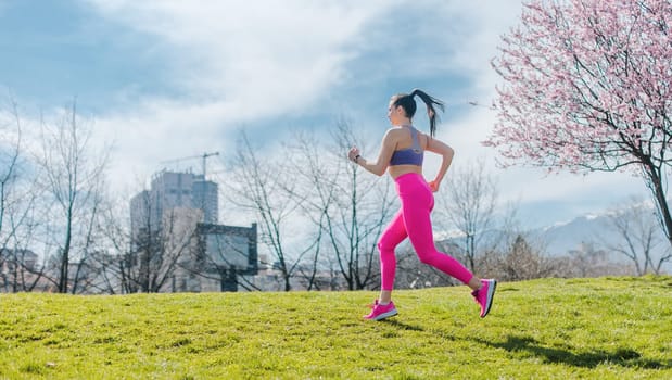 Sportive girl running in park on spring day in front of blossom