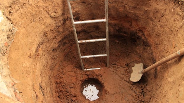 water at the bottom of a newly dug well, top view, in the well, a digger's tool, a shovel and a ladder