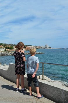 Two children stand on the promenade and look at the sea, on the Côte d'Azur in France