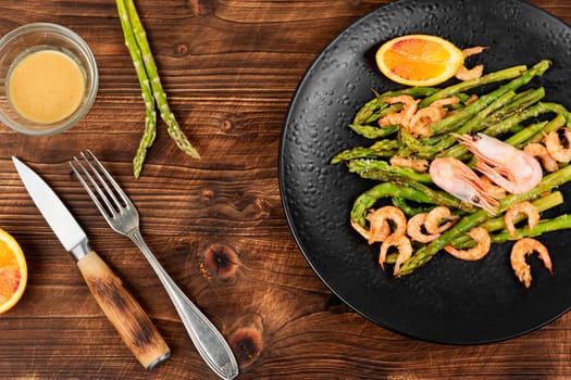 Roast asparagus with fried prawns on rustic wooden table. Top view, copy space.