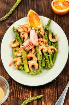Roast asparagus with fried prawns on rustic wooden table. Top view, copy space.