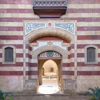 Striking red and white striped arched entrance leads into a Mamluk era style building, showcasing intricate architectural details