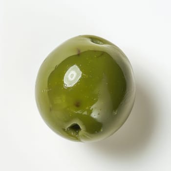 A single green olive sits on a white background. The olive is smooth and slightly wrinkled, with a small stem attached