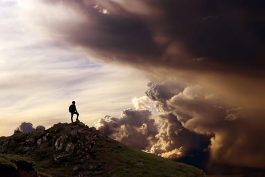 A man stands on a mountain and looks into a fantastic cloudscape
