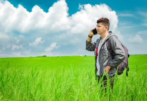 Man calling by cell phone, young man in the field calling by cell phone, young backpacker with cell phone in the field and copy space